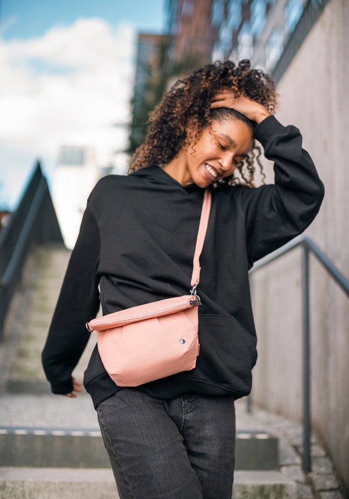 Woman carrying the Pacsafe Citysafe CX Anti-Theft Convertible Crossbody color Rose made with ECONYL® regenerated nylon