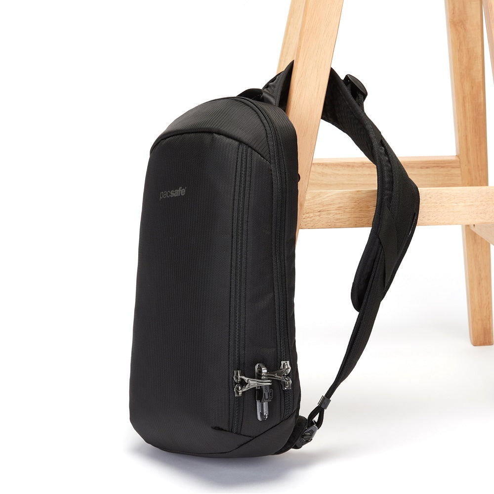 Side view of the Pacsafe Vibe 325 Anti-Theft Sling Pack color Black made with ECONYL® regenerated nylon locked to a chair