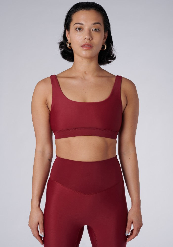 Front view of a woman wearing the Mera Sports Bra Wine by Outfyt color Red made with ECONYL® regenerated nylon