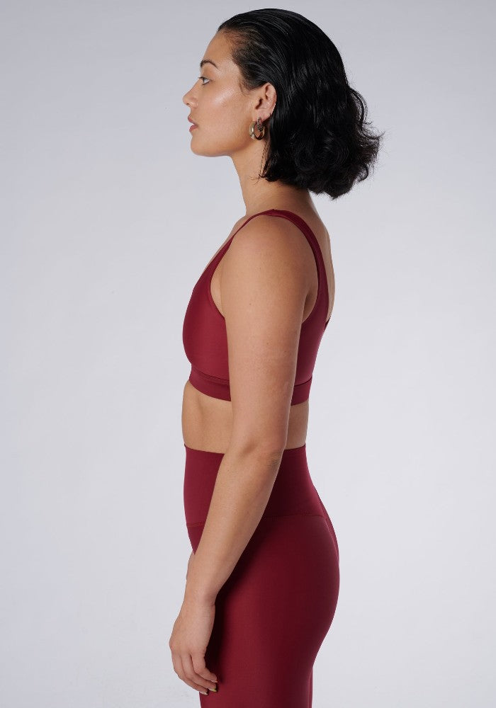 Side view of a woman wearing the Mera Sports Bra Wine by Outfyt color Red made with ECONYL® regenerated nylon