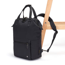Load image into Gallery viewer, Side view of the Pacsafe Citysafe CX Anti-Theft Mini Backpack color Black made with ECONYL® regenerated nylon locked to a chair

