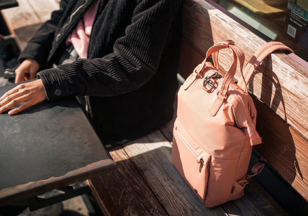 Woman sitting with the Pacsafe Citysafe CX Anti-Theft Mini Backpack color Rose made with ECONYL® regenerated nylon