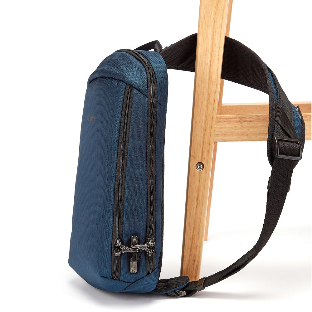 Side view of the Pacsafe Vibe 325 Anti-Theft Sling Pack color Ocean made with ECONYL® regenerated nylon locked to a chair